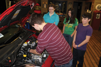 Students look under the hood of a car while they learn to change their own oil at a program sponsored by a local Fiat dealer.