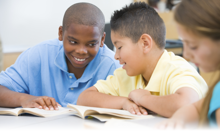 Language Learning: Two boys at desk reading and sharing a book.