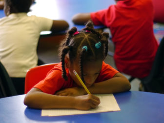 Young girl in Robert Bowne Foundation funded afterschool program writing at desk