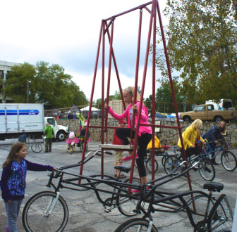A girl climbs onto a swing at the top of two bicycles. The structure was created by kids in the youth development program Art 120. 