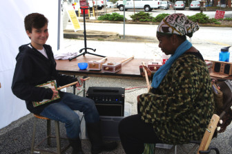 Patrick Wright, 14, makes guitars from cigar boxes. Here, he plays music with a visitor to his booth at Maker Faire Atlanta. 