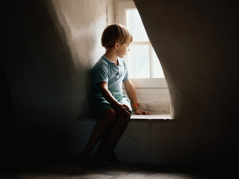 Boy (6-7) sitting on window sill, looking out window