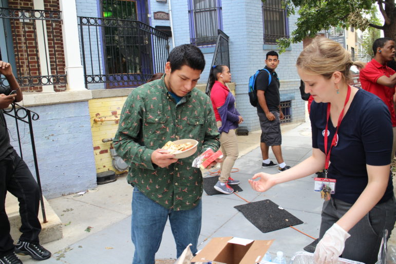 Jesus Gutierrez receives a slice of watermelon from LAYC community schools coordinator Carolyn Greenspan as people line up for quesadillas at the Seva Food Truck, which partners with LAYC. 