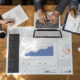 Data: hands of people sitting around conference table typing on laptops, writing notes while studying data chart on table