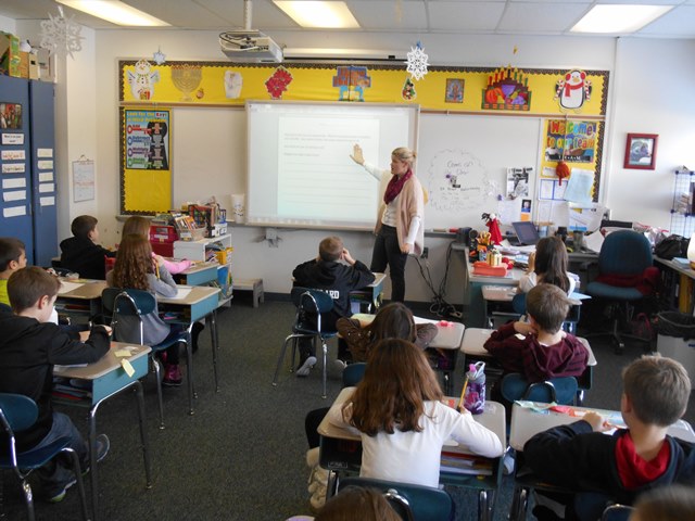 Nora Gajewski, standing at front of classroom, gestures to slide on screen in front of children at desks. She is coordinator of the before-and after-school program at the Bassett Elementary school for Project Link of the Westlake K-12 School District in Westlake, Ohio.