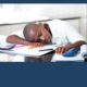 Sleep deprivation AASM study says low-income teens of color more affected: Black teen boy sleeps on school desk with head on notebook.