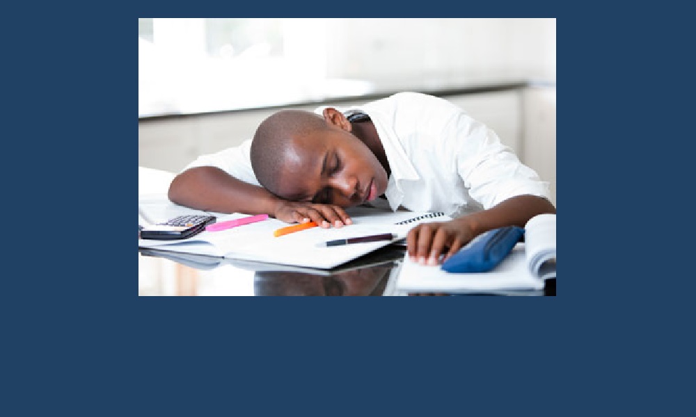 Sleep deprivation AASM study says low-income teens of color more affected: Black teen boy sleeps on school desk with head on notebook.