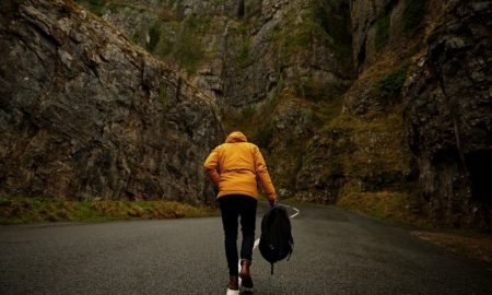 Fute uncertain for person in orange coat walking alone with backback on road surrounded by mountains