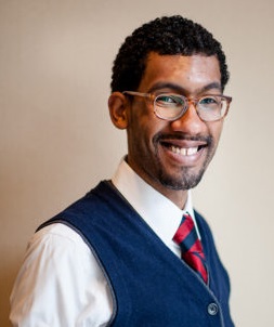 Trey Rabun (headshot), family outreach specialist for Amara, smiling man with beard, mustache, wearing glasses, blue vest, white shirt, red and blue tie.