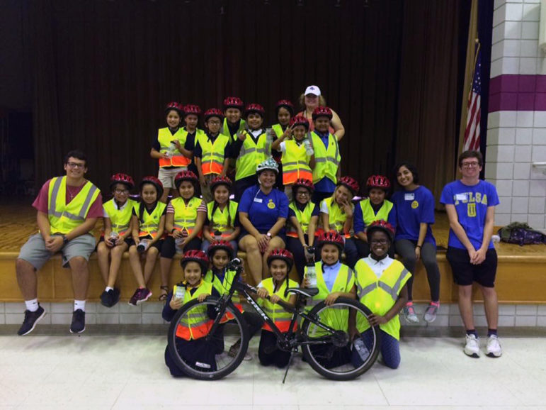 21st Century after-school program: A group of young boys and girls in yellow safety vests and bike helmets smile proudly, posing with a bicycle and five adults.