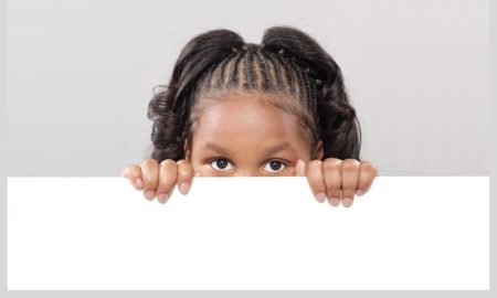 OPINION Young black girl peers over empty white space grasping top edge with hands