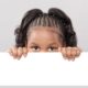 OPINION Young black girl peers over empty white space grasping top edge with hands