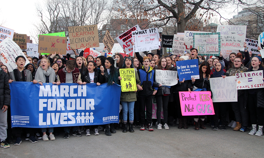 Student activists hold large blue March for Our Lives banner with crowd of young people holding signs.