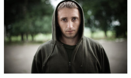 Violence: youth in olive green hooded sweatshirt looks lost, isolated, sad.