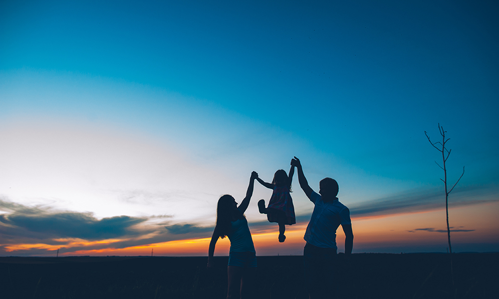 Adults holding small child up before a setting sun