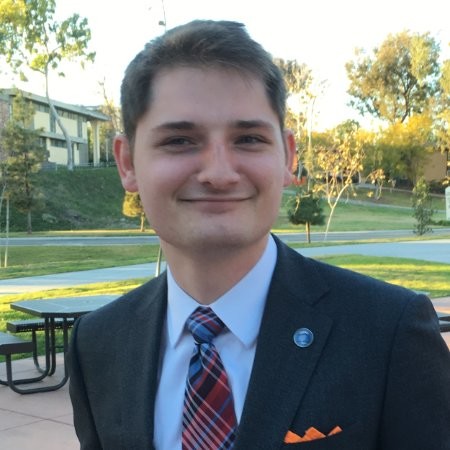 Conservatives: Aaron Van Meter-Jones (headshot), college student, smiling man in dark suit, light blue shirt, plaid tie, orange pocket square.