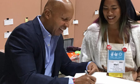 Bryan Stevenson: Smiling bald man in light blue shirt, dark blue jacket signs book for smiling woman with long dark hair in white jacket, dress, with ID badge around her neck.
