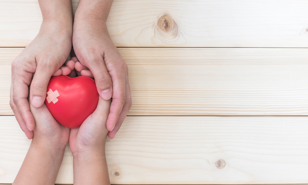 Adult hands holding child's hands holding an apple over wooden boards.