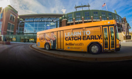 Afterschool: Ad-wrapped yellow bus in front of Lambeau Field Atrium.
