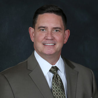 Foster care: Bobby Cagle (headshot), director of Los Angeles County’s Department of Children and Family Services, wearing olive suit, white shirt, olive patterned tie.