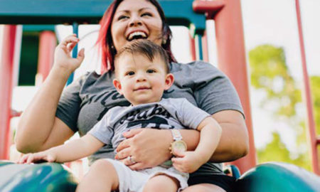 Kids Count: Laughing woman holds toddler as they go down slide.