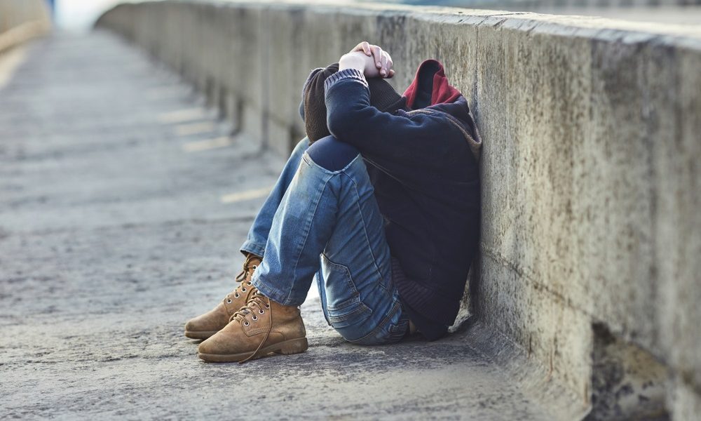 youth homelessness: young person sitting with head in hands on side of a street