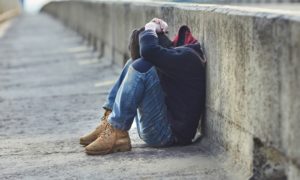 runaway and homeless youth grants: young person sitting with head in hands on side of a street