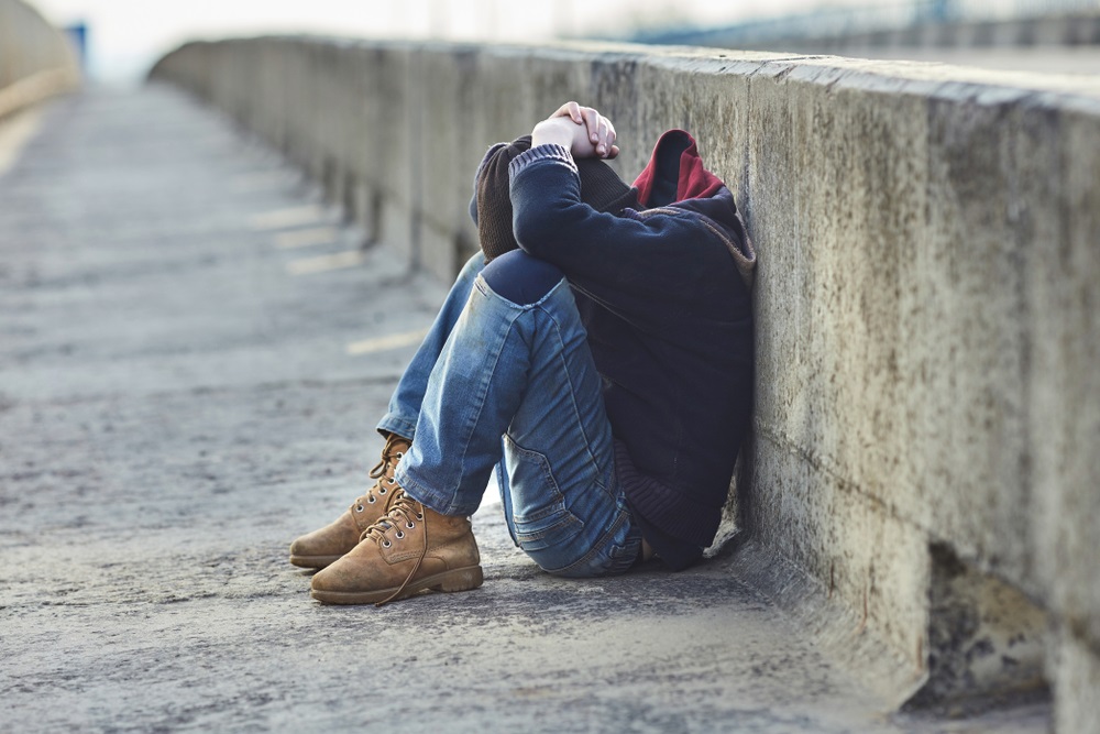 youth homelessness: young person sitting with head in hands on side of a street