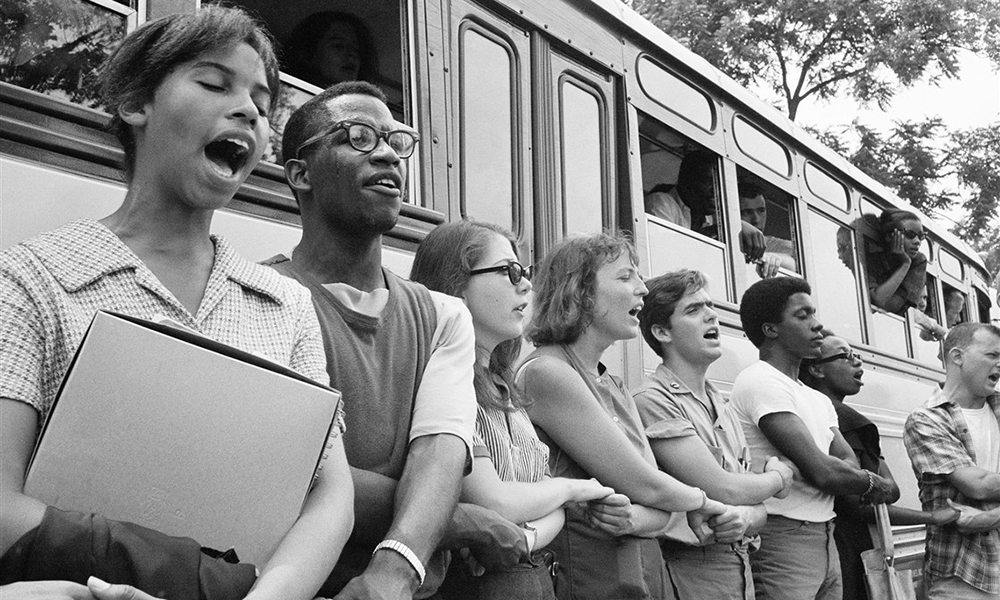 Youth leaders: Young black and white activists hold hands in front of school bus in historic photo from 1964 Mississippi.