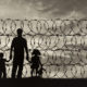 Immigrants: Silhouette of a family with children of refugees and fence with barbed wire in background.