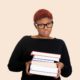 Microaggressions: Closeup portrait of young sad woman, student wearing big glasses, holding pile of books, anxious unhappy, isolated on white background.