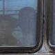Immigration: Little boy barely seen through bus dark window.