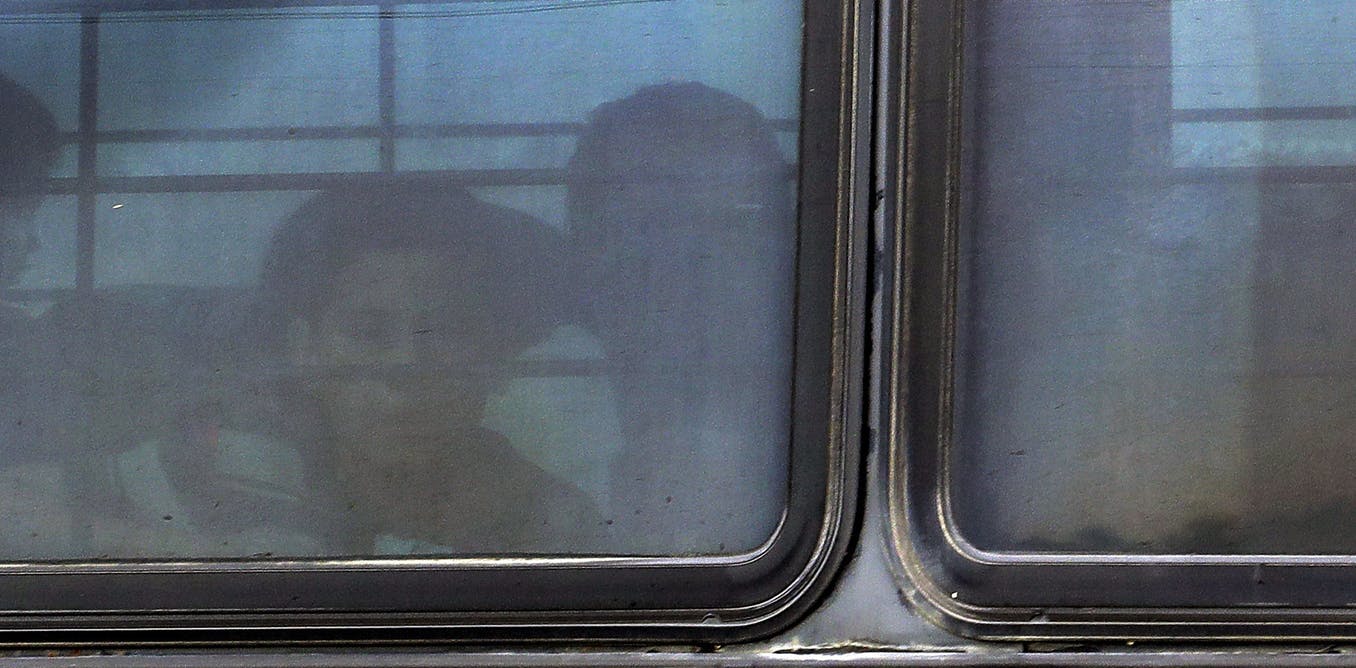 Immigration: Little boy barely seen through bus dark window.