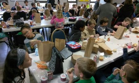summer meals: children eat food from paper bags at long tables.