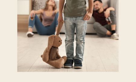foster care: Little boy holding toy bunny while his parents drink alcohol in background