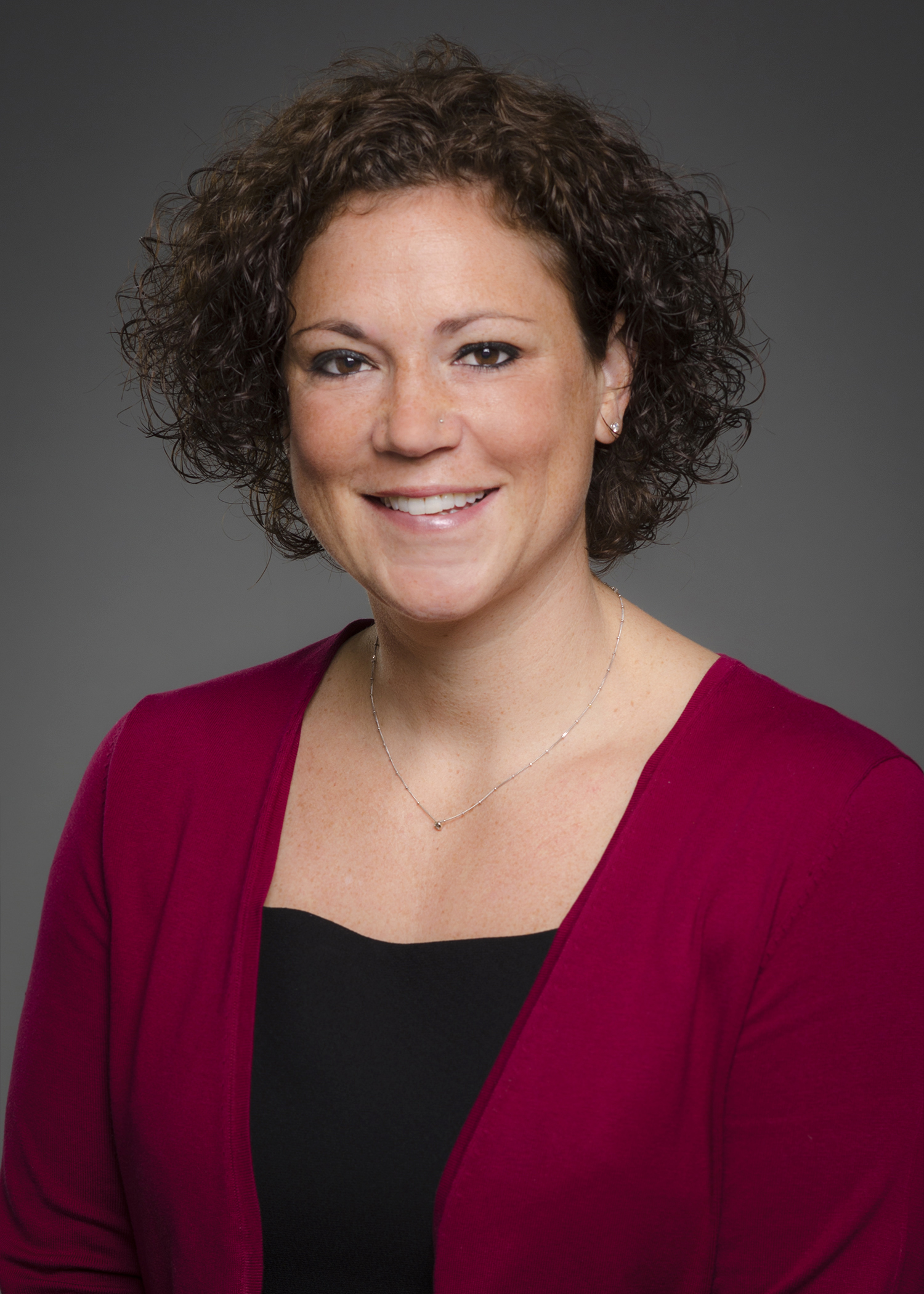 social and emotional learning: Nicole Lovecchio (headshot), chief programming officer at WINGS for Kids, smiling woman with short brown curly hair, earrings, necklace, black top, maroon jacket.