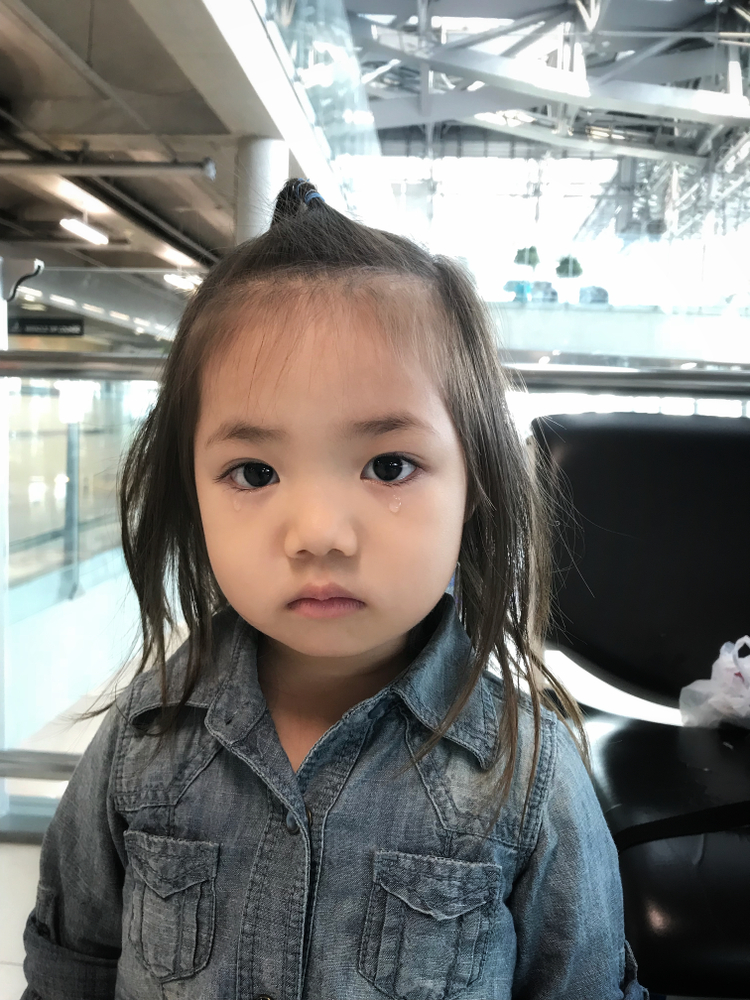 immigration: Adorable toddler baby with Jeans shirt crying and expressions of sadness. Little asian cute girl with in the eyes visible tears sitting in the airport international.