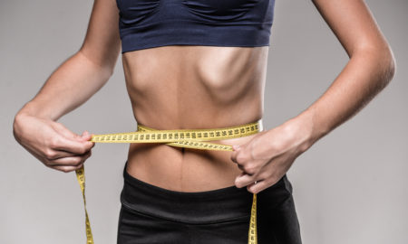 eating disorder: Young skinny woman with ribs sticking out is measuring her waist during diet.