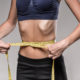 eating disorder: Young skinny woman with ribs sticking out is measuring her waist during diet.