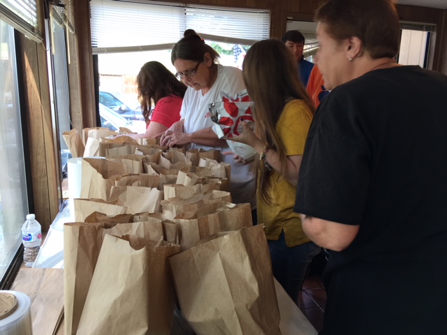 summer meals: People stand next to table full of paper bags standing up.