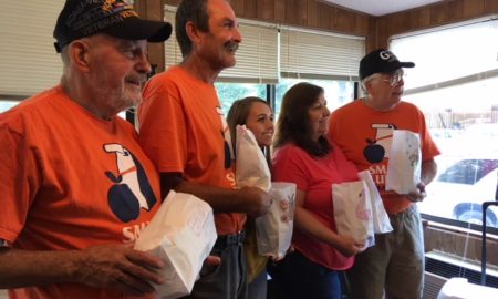 summer meals: 5 men and women in orange T-shirts stand in line facing out holding paper bags.