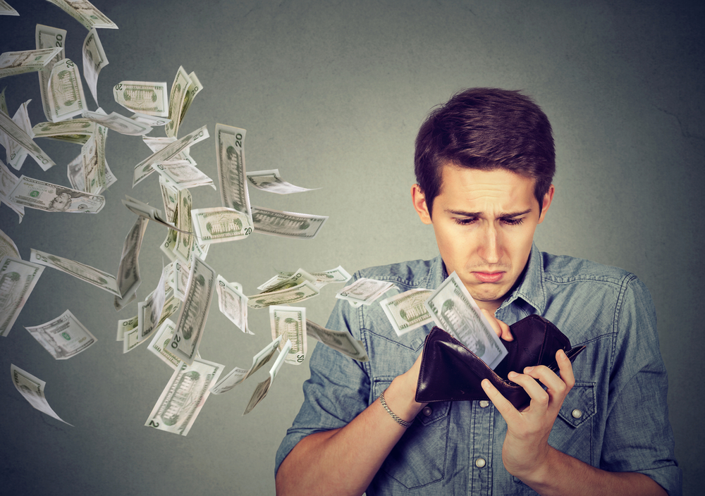 scarcity mindset: Sad man looking at his wallet with money dollar banknotes flying out away