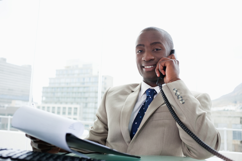 fundraising: Smiling businessman on the phone while reading a document in his office