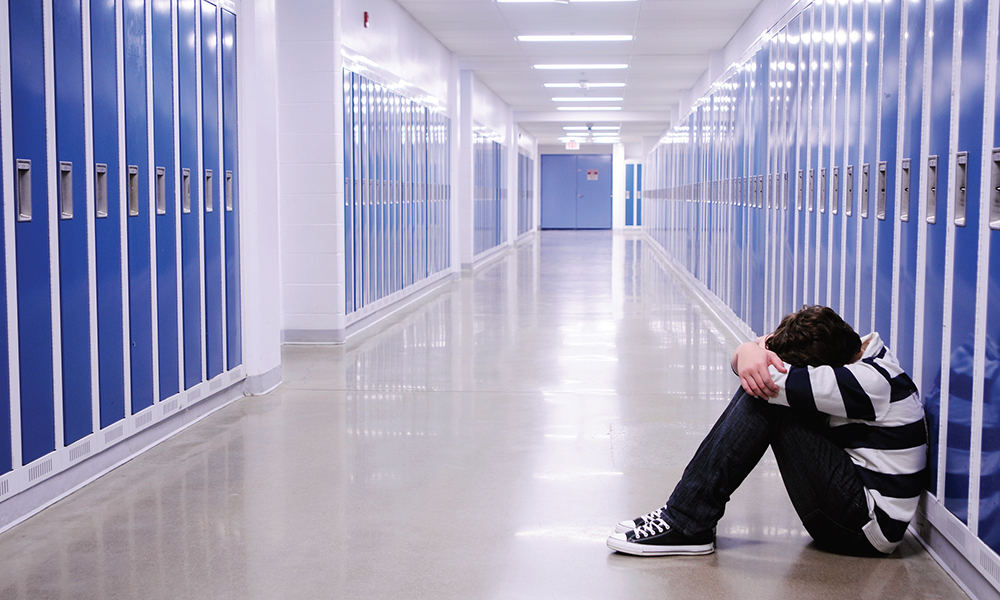 social and emotional learning: student sitting on floor of school hallway against lockers, head buried on knees.