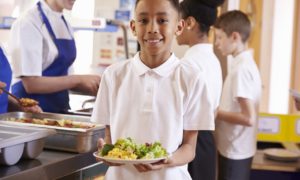 farm to school program grants: young boy holding school lunch plate while smiling