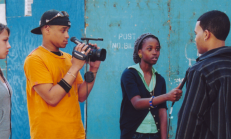 poverty: 4 young people: woman wearing headphone, man holding camera, woman holding microphone up to another man