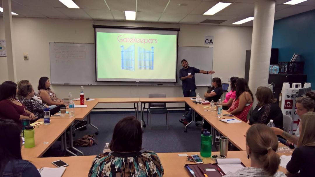 undocumented: Students sit at rectangular table in college classroom; image of open gates shown on wall