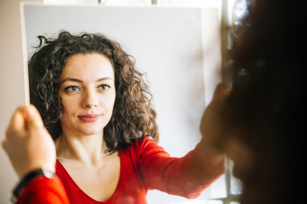 equity: Woman with curly hair standing in front of large mirror