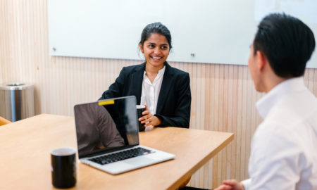 professional development plan: A young Indian Asian woman has a meeting or interview with a Chinese manager in a meeting room during the day. They are professionally dressed and she is smiling genuinely as she speaks.