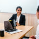 professional development plan: A young Indian Asian woman has a meeting or interview with a Chinese manager in a meeting room during the day. They are professionally dressed and she is smiling genuinely as she speaks.